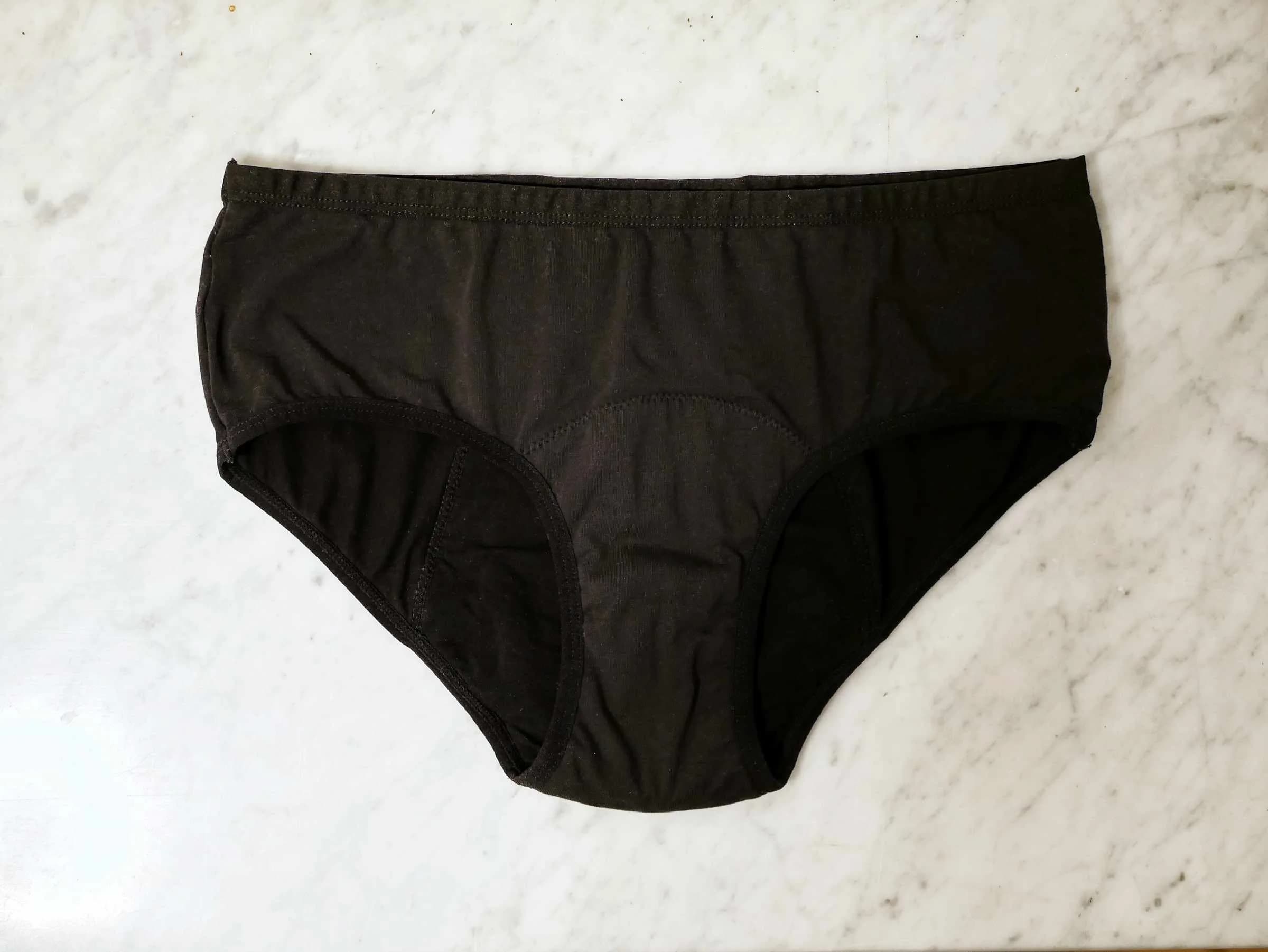 Black period underwear laid flat on white marble