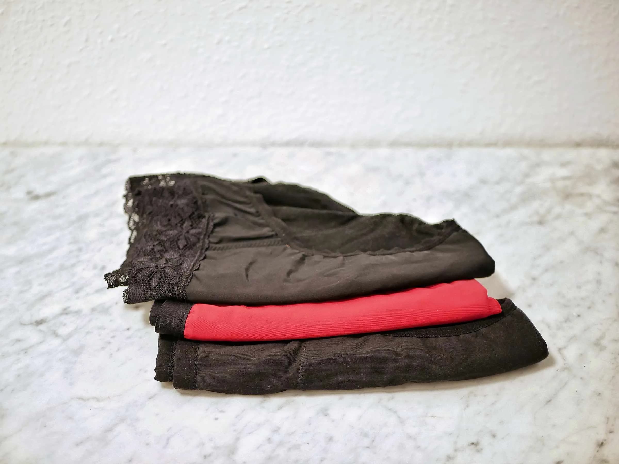 Folded period underwear in black and red stacked on marble
